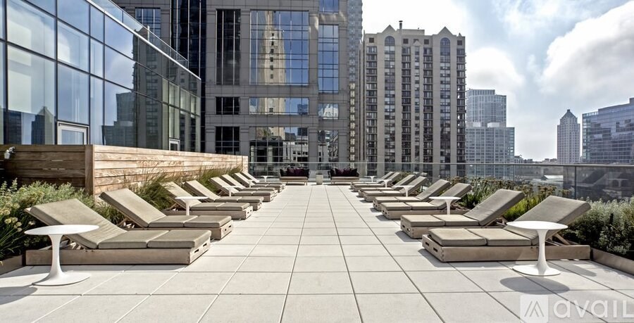 A rooftop patio with lounge chairs and tables overlooking a city skyline.