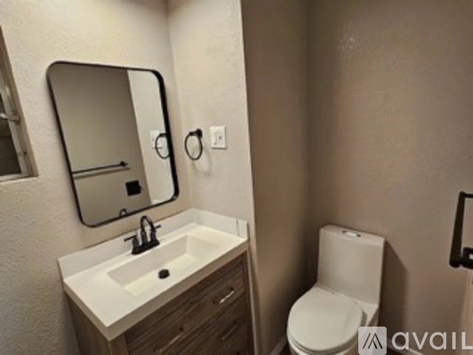 A bathroom with a sink, mirror, toilet and a black frame on the wall.