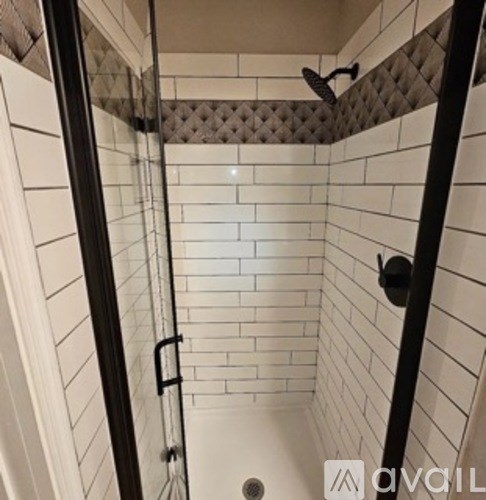 A white tiled shower with a black handle.