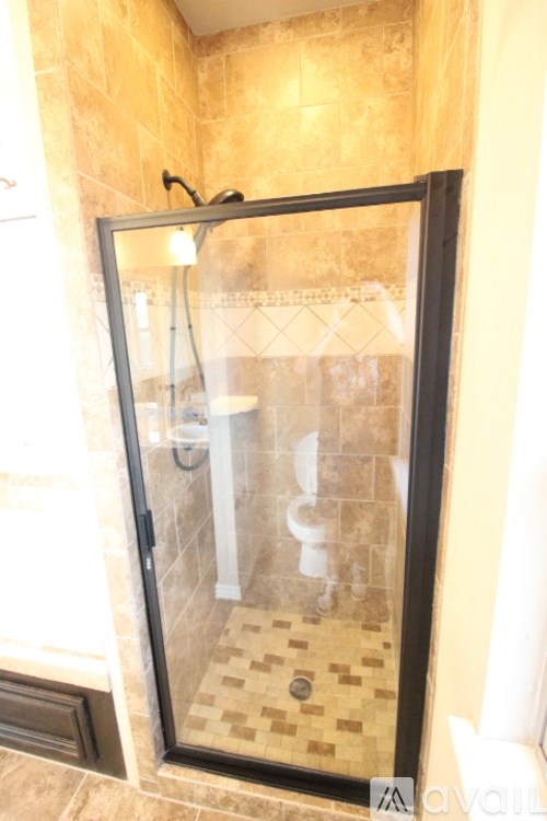 A shower with a glass door is in a bathroom with tiled walls.
