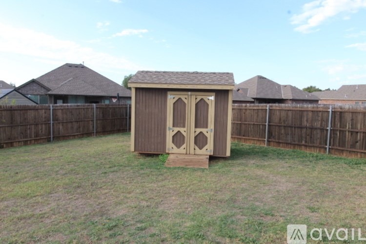 A small wooden structure with a brown roof and two doors is situated in a grassy area.