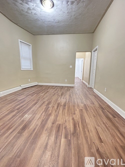 A room with wooden flooring and a window on the left wall.