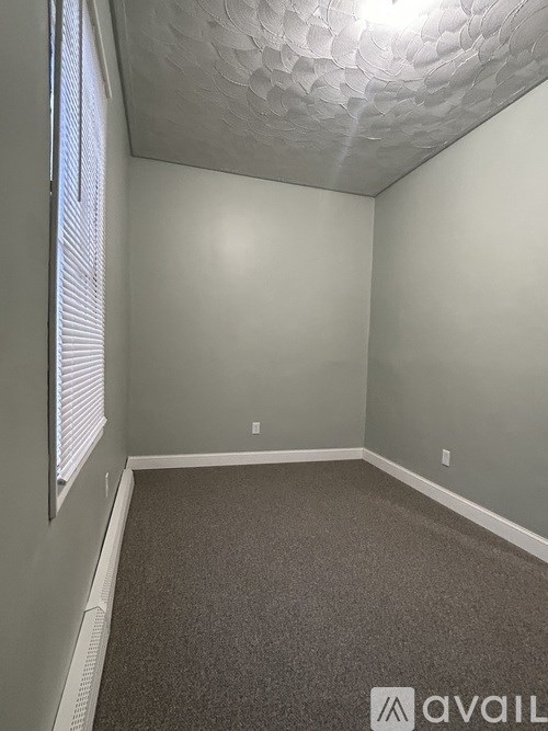A room with a carpeted floor and a window with blinds.