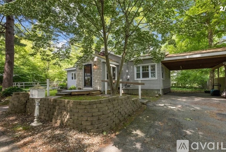 A house with a stone wall and a porch is surrounded by trees.