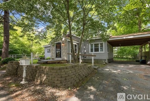 A house with a stone wall and a porch is surrounded by trees.