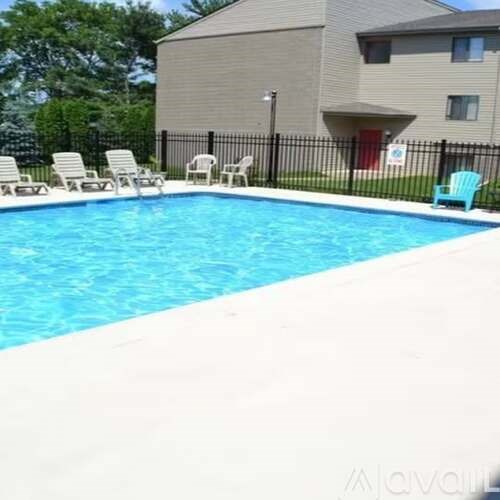 A swimming pool with chairs around it and a building in the background.