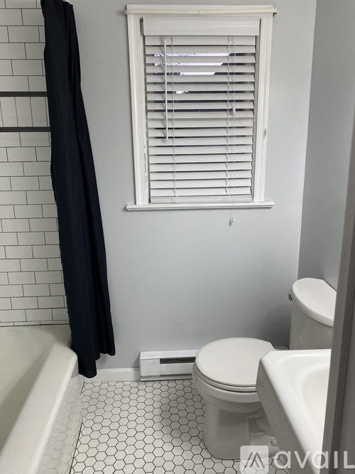 A white toilet sits next to a white bathtub in a bathroom with a black shower curtain.