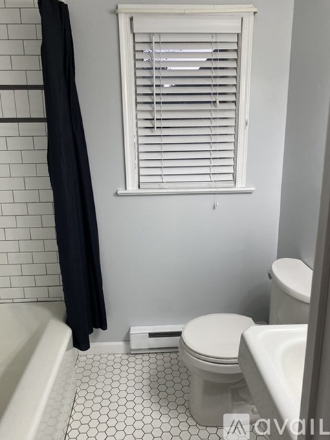 A white toilet sits next to a white bathtub in a bathroom with a black shower curtain.