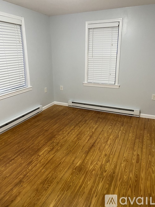 A room with wooden flooring and two windows with blinds.