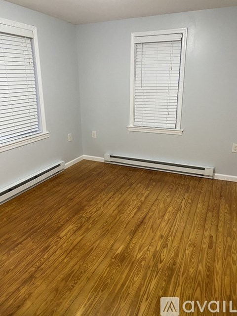 A room with wooden flooring and two windows with blinds.