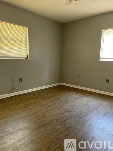 A room with wooden flooring and two windows.