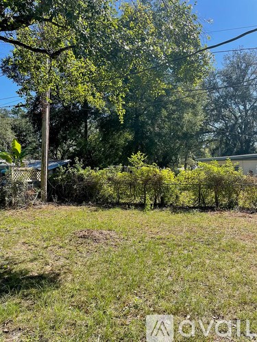 A field with trees and a house in the background.