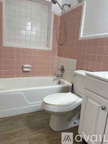 A white toilet sits in a bathroom with pink tiles.