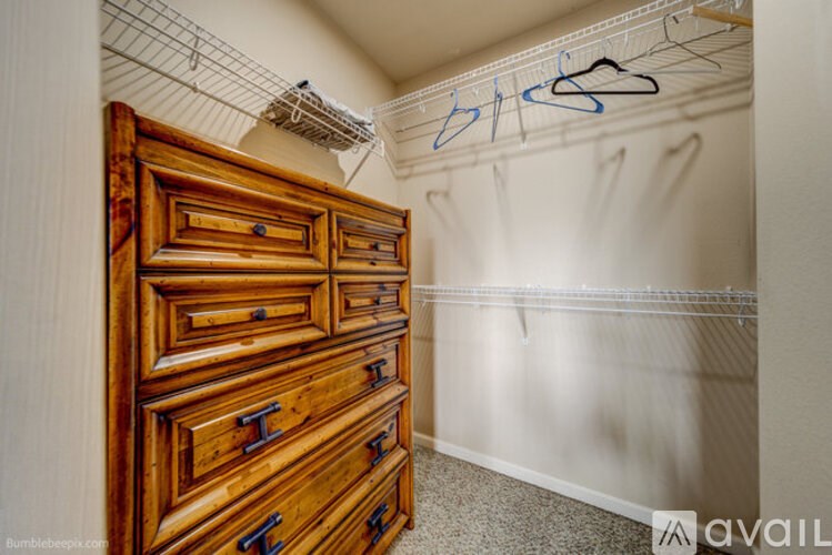 A wooden chest of drawers in a room with a white wall and a clothes rack.