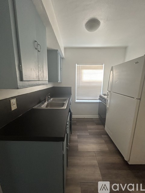 A kitchen with a white fridge and a window with blinds.