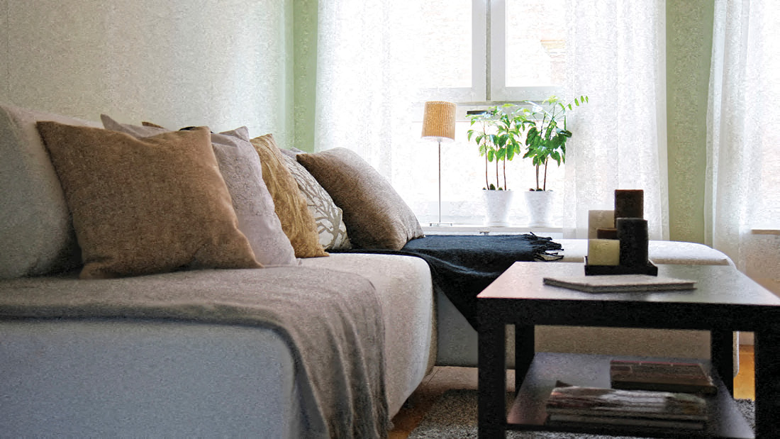 A living room with a grey couch and a small table with a plant on it.