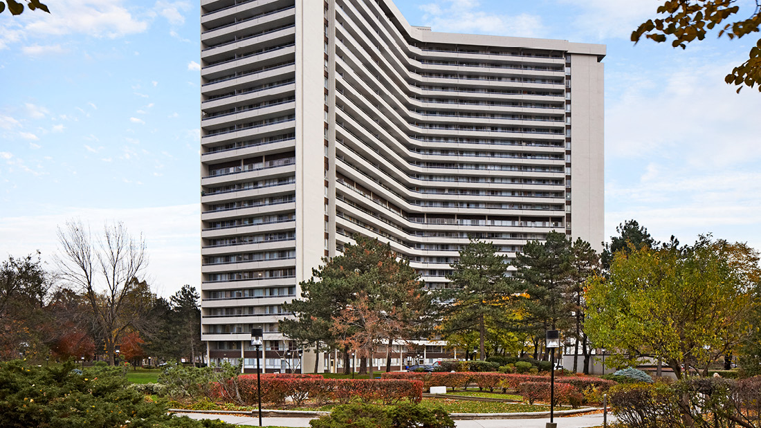 A tall building with a striped facade is surrounded by trees and shrubbery.