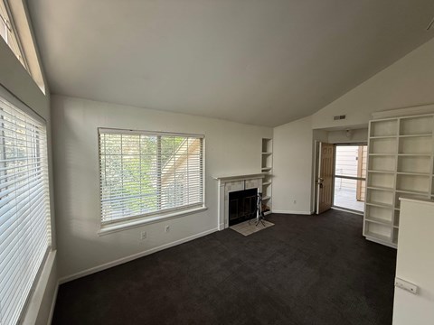 A living room with a fireplace and a window with blinds.