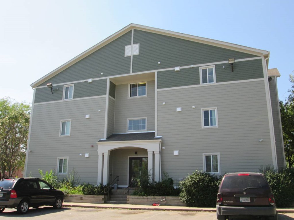 A grey two story building with a car parked in front.