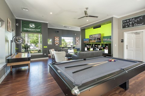 A pool table is in the middle of a room with a green wall and a sign that says "Sacramento State.".