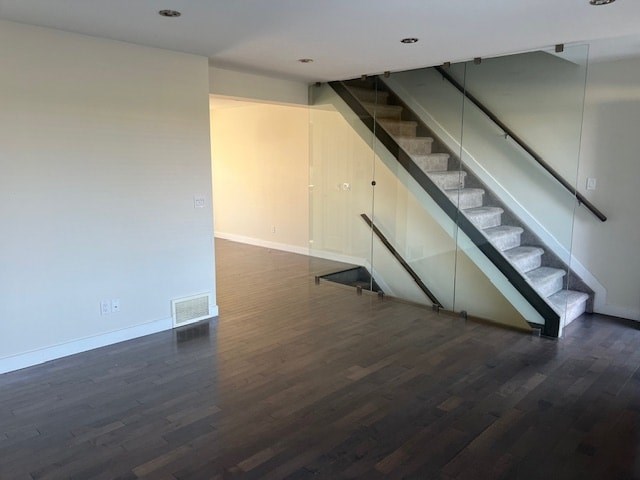 A room with a wooden floor and a staircase with glass railings.