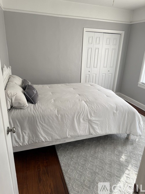 A white bed with a white pillow and a white bedspread in a room with a white door.