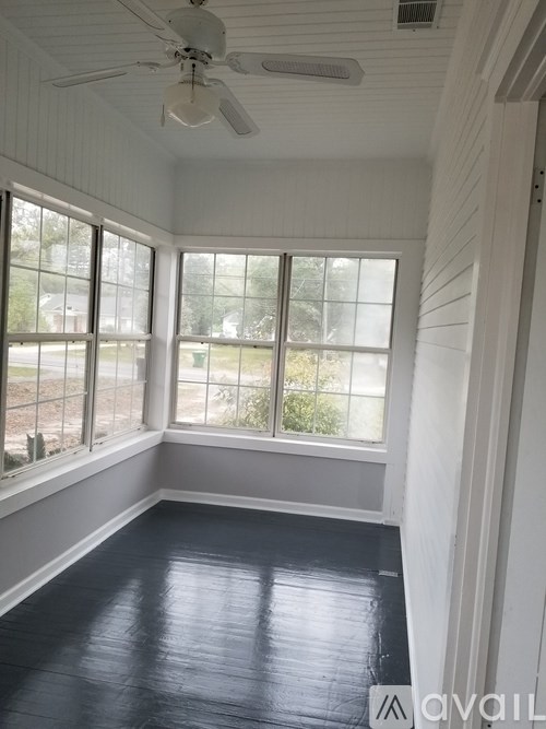 A room with a ceiling fan and large windows.