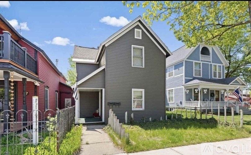 A house with a grey exterior is in the foreground with a red house to its left and a blue house to its right.