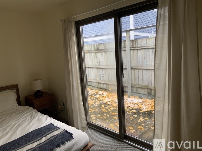 A bedroom with a bed, nightstand, and a view of a backyard through a sliding glass door.