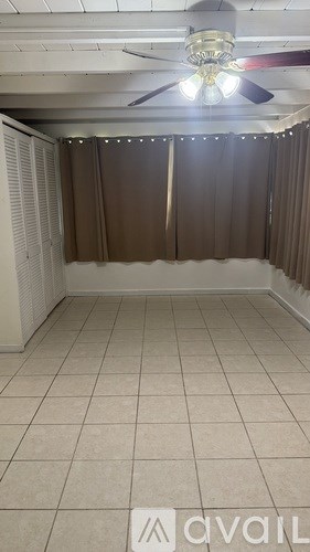 A room with a ceiling fan and a window with curtains.