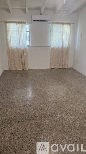 A room with a carpeted floor and two windows with curtains.