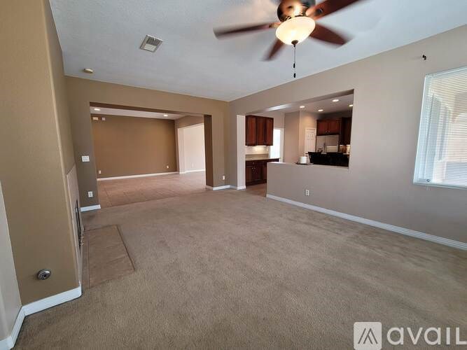 A spacious living room with a ceiling fan and carpeted floor.