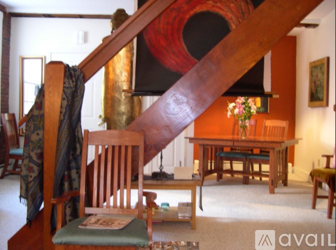 A wooden chair with a green cushion is in the foreground of a room with a wooden staircase.