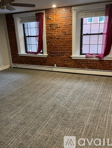 A room with a carpeted floor and two windows with red curtains.