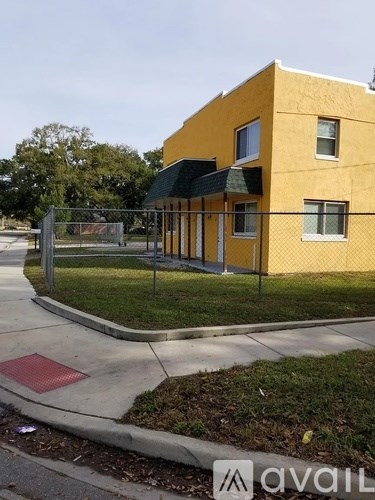 A yellow building with a black awning and a metal fence in front.