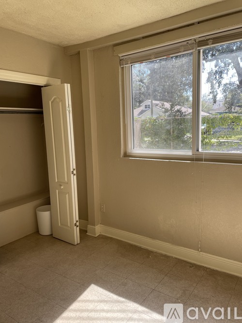 A room with a door open to a hallway and a window with a view of a house and trees outside.