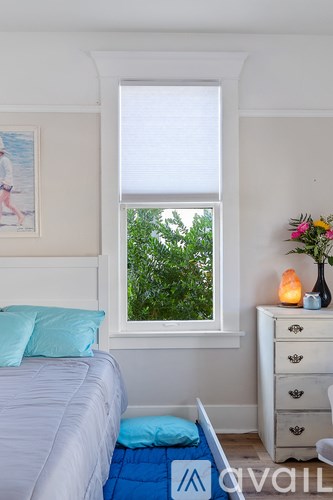 A bedroom with a bed, dresser, and a window with a view of greenery outside.