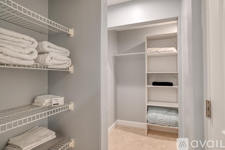 A bathroom with towels on the shelf and a bed in the corner.