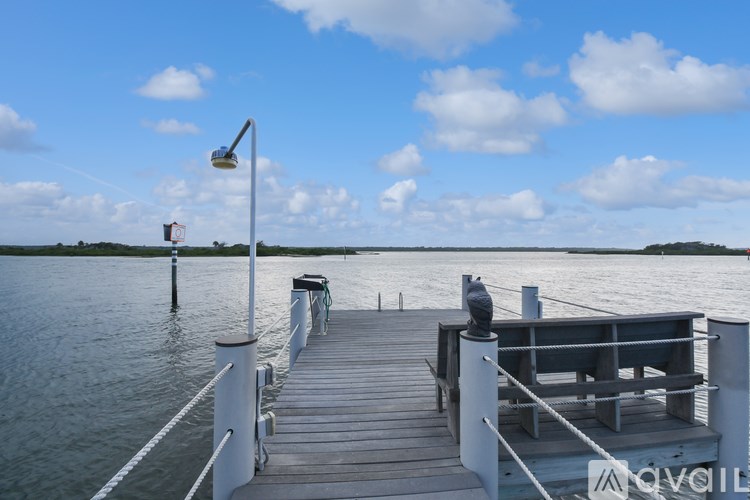 A wooden dock extends into a calm body of water under a blue sky with scattered clouds.