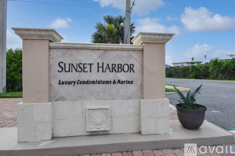 A sign that says Sunset Harbor stands in front of a street.