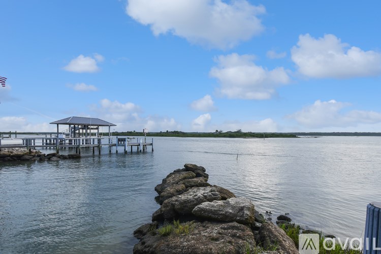 A pier extends into a calm body of water with a cloudy sky above.