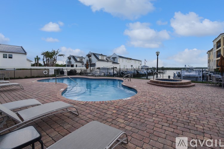 A pool surrounded by a brick patio with chairs and a fence.