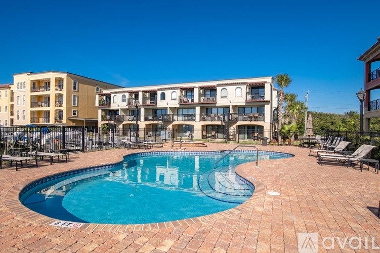 A large outdoor swimming pool surrounded by a brick patio and lounge chairs.