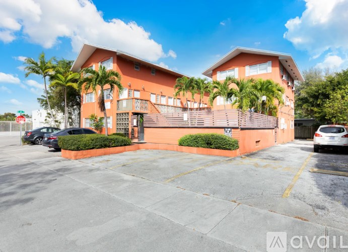 A building with a balcony and a parking lot in front.