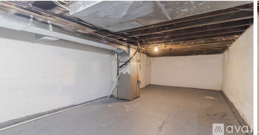 A room with a concrete floor and walls, with a door and a window, and some pipes on the ceiling.