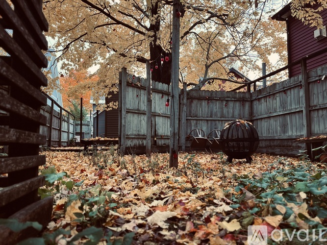 A wooden fence with a gate and a tree with brown leaves.