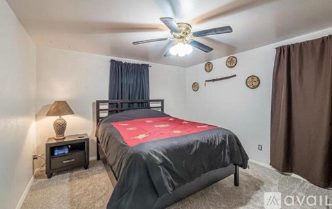 A bedroom with a bed, a ceiling fan, and a nightstand with a lamp.