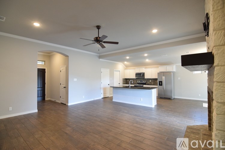 A spacious living room with a kitchen in the background and a ceiling fan in the middle of the room.