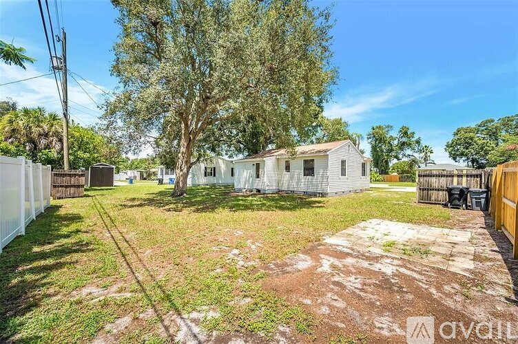 A backyard with a tree, a fence, and a house.