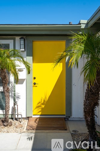 A yellow door is flanked by two palm trees.
